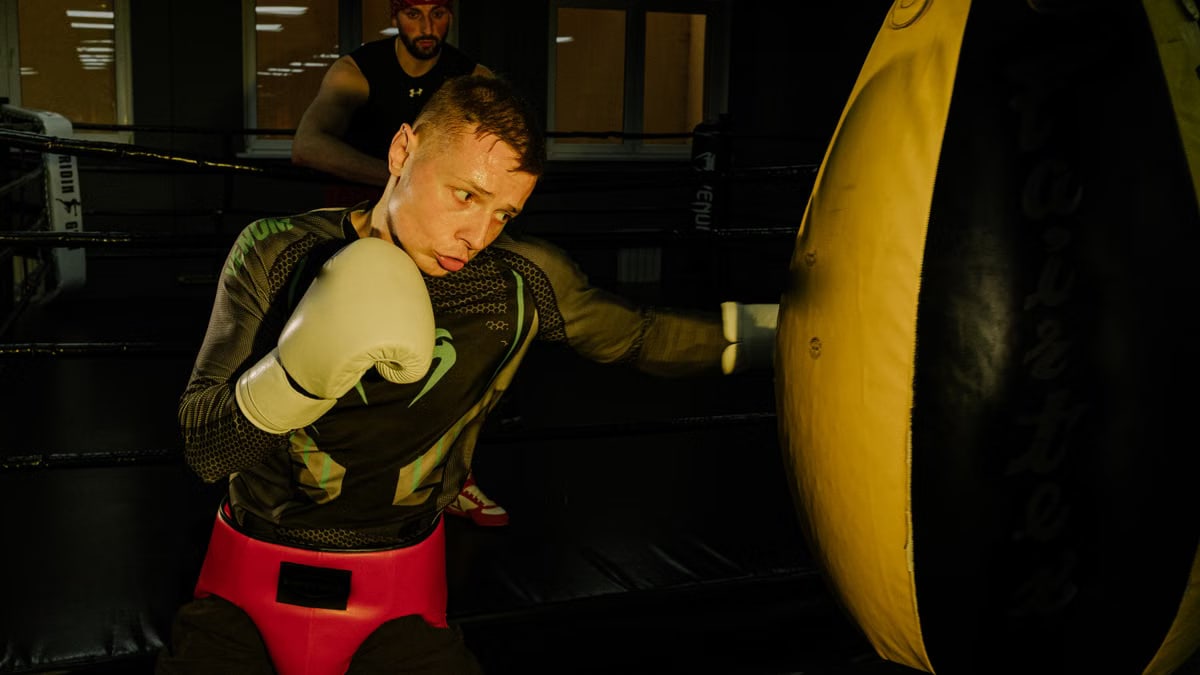 A determined boxer practicing punches on a heavy bag with a trainer in the gym.